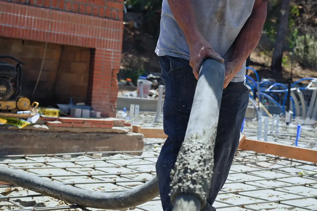 A VR Plumbing Inc and Construction crew member guiding the concrete pump hose over the rebar grid of the foundation