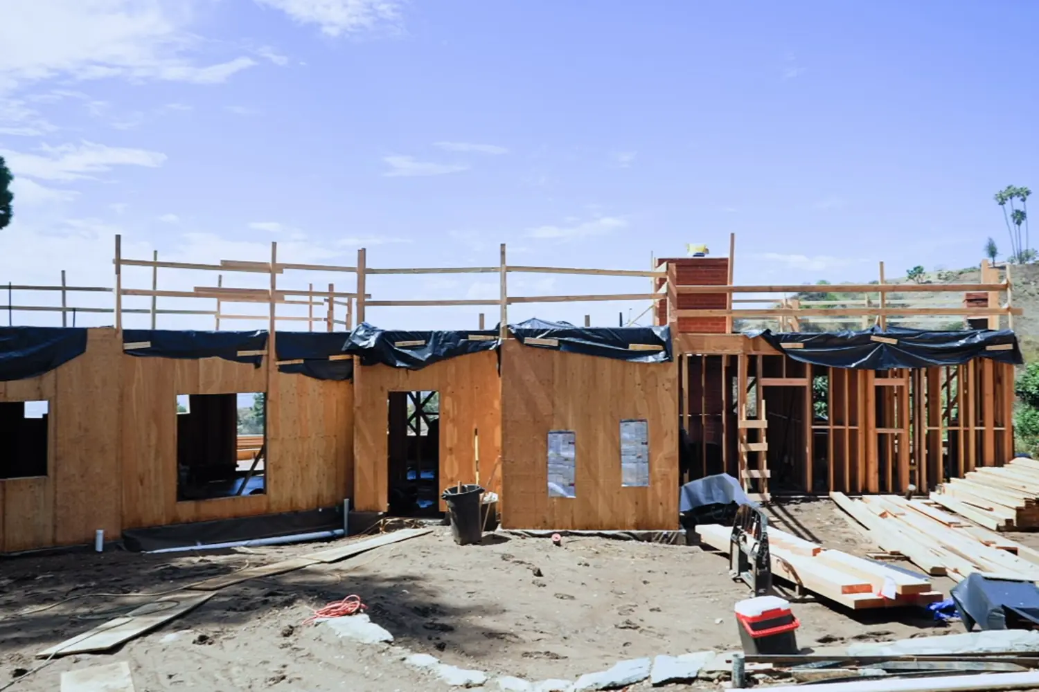The exterior walls of a house framed in lumber under a blue sky, scaffolding along the top plate