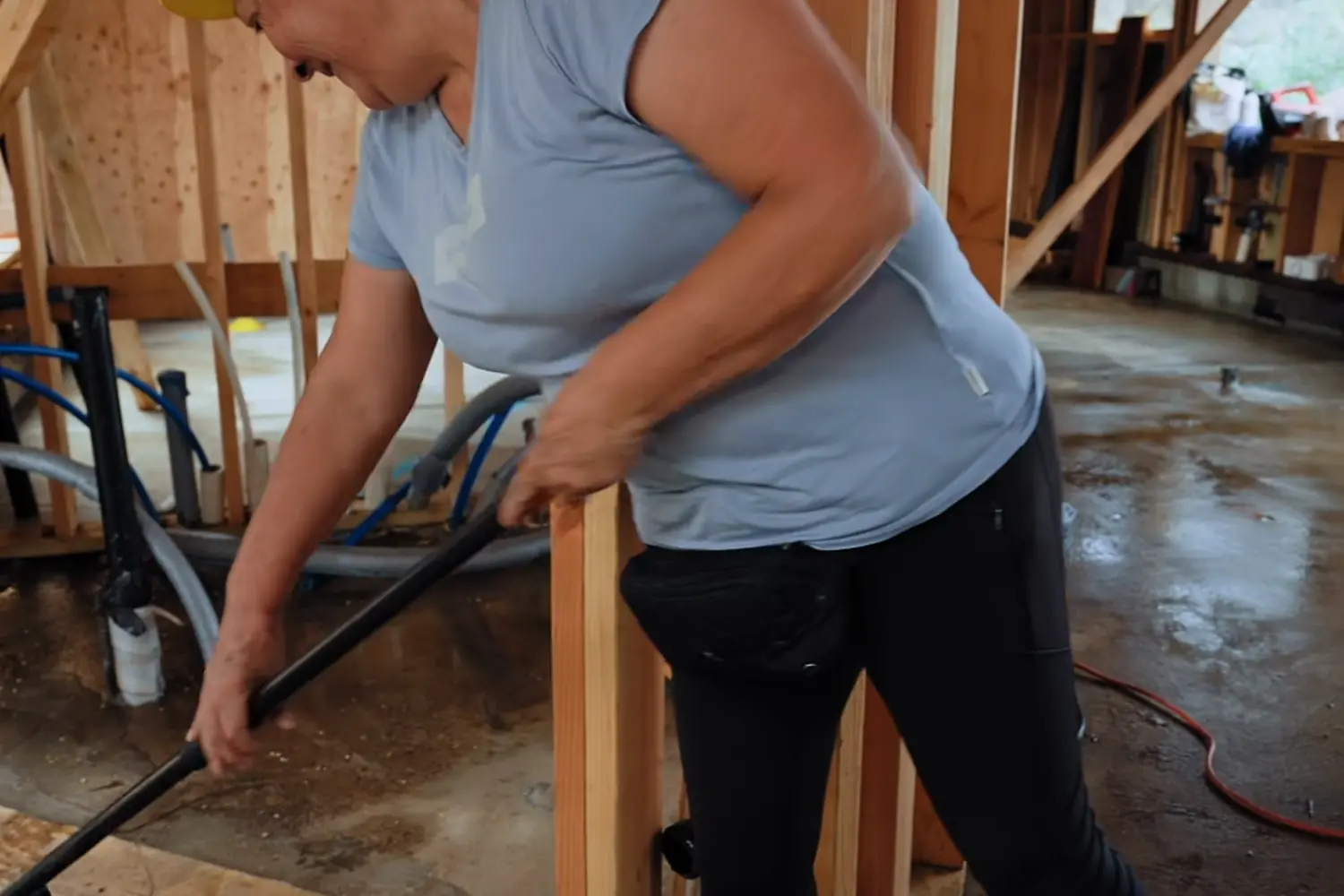 A crew member sweeping the concrete floor of a framed house before leaving the site